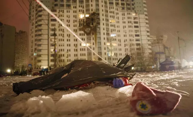 The dead body of a paramedic lies on the ground in front of a residential building damaged by a Russian strike on Kyiv, Ukraine, Friday, Jan. 9, 2026. (AP Photo/Evgeniy Maloletka)