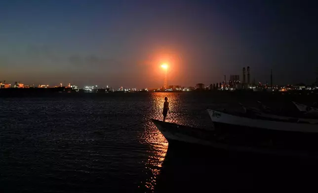 A boy stands on a fishing boat with the Cardon refinery in the background in Punta Cardon, Venezuela, Wednesday, Jan. 14, 2026. (AP Photo/Matias Delacroix)