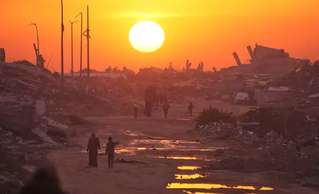 Palestinians walk through the ruins of destroyed buildings as the sun sets over Gaza City, Sunday, Jan. 4, 2026. (AP Photo/Jehad Alshrafi)