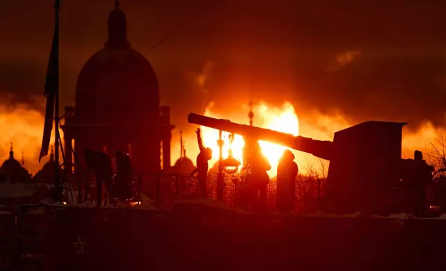 People walk during sunset near the front deck gun of the Aurora Cruiser which crew members in Oct. 1917 used to fire a blank shot giving the signal to begin the Bolshevik Revolution, in St. Petersburg, Russia on Monday, Jan. 5, 2026. (AP Photo/Dmitri Lovetsky)