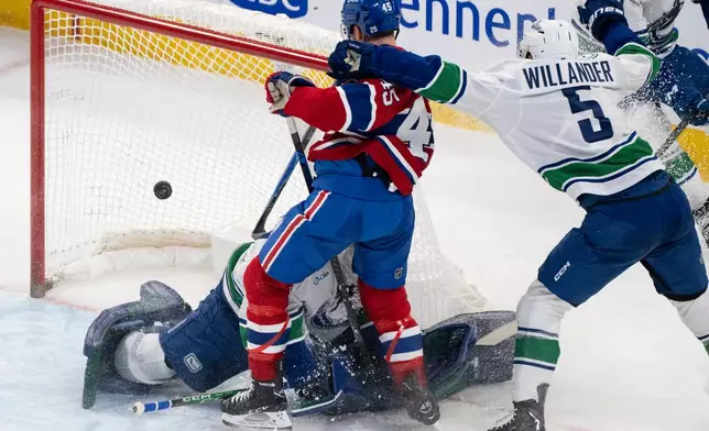 Montreal Canadiens' Alexandre Carrier (45) scores against Vancouver Canucks goaltender Nikita Tolopilo, bottom left, as Canucks' Tom Willander (5) defends during second-period NHL hockey game action in Montreal, Monday, Jan. 12, 2026. (Christinne Muschi/The Canadian Press via AP)