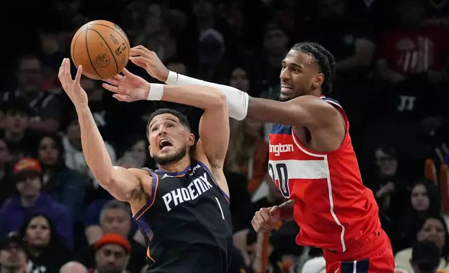 Phoenix Suns guard Devin Booker (1) and Washington Wizards center Alex Sarr battle for a loose ball during the first half of an NBA basketball game, Sunday, Jan. 11, 2026, in Phoenix. (AP Photo/Ross D. Franklin)