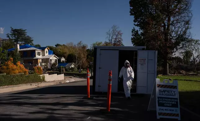 A worker in protective gear exits a storage container at a cleanup site, Dec. 3, 2025, months after the Eaton Fire, in Altadena, Calif. (AP Photo/Jae C. Hong)