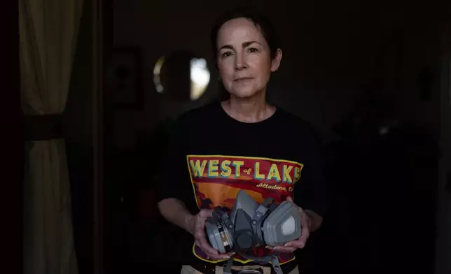 Nina Malone, whose home survived the Eaton Fire, stands for a photo with a respirator she uses when cleaning fire debris inside her home, Dec. 11, 2025, in Altadena, Calif. (AP Photo/Jae C. Hong)
