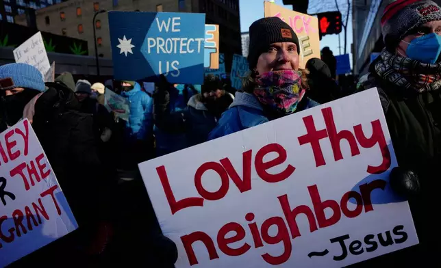 A protester holds a sign reading "Love thy neighbor - Jesus" during a rally against federal immigration enforcement on Friday, Jan. 23, 2026, in Minneapolis. (AP Photo/Angelina Katsanis)