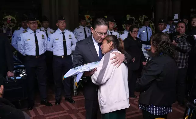 Interior Minister Marco Antonio Villeda gives a Guatemalan flag to the mother of police officer Luis Zetino, one of many officers killed while retaking control of three prisons, during a wake for the fallen officers at the Interior Ministry in Guatemala City, Monday, Jan. 19, 2026. (AP Photo/Moises Castillo)