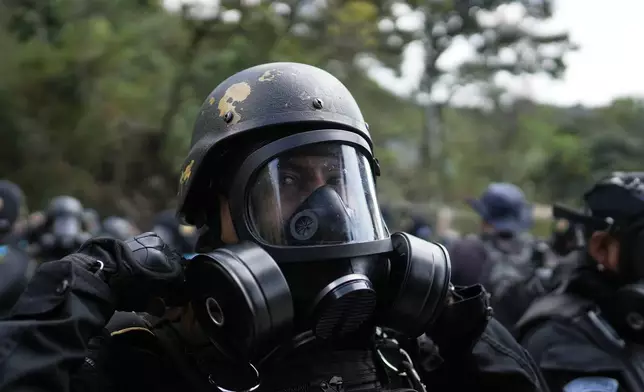 An anti-riot policeman adjusts his gas mask outside the Preventivo Zona 18 prison during a operation to free guards taken hostage and retake control of the facility in Guatemala City, Sunday, Jan. 18, 2026. (AP Photo/Emmanuel Andres)
