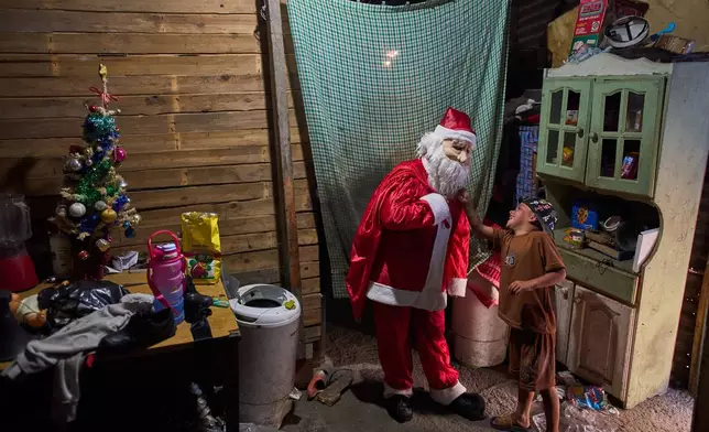 FILE - Cinthia Falcón, a neighbor dressed as Santa Claus, delivers gifts donated by NGOs during a celebration organized by a neighborhood soup kitchen in Lomas de Zamora, a suburb of Buenos Aires, Argentina, Dec. 27, 2025. (AP Photo/Rodrigo Abd, File)