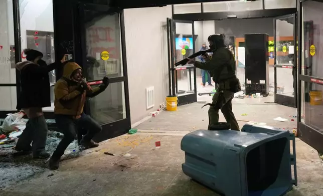 A federal agent points a weapon at a person outside a hotel during a noise demonstration protest in response to federal immigration enforcement operations in the city Sunday, Jan. 25, 2026, in Minneapolis. (AP Photo/Adam Gray)