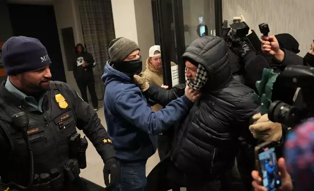 A man, center left, next to a Minneapolis police officer grabs a protester in the doorway during a noise demonstration protest in response to federal immigration enforcement operations in the city Sunday, Jan. 25, 2026, in Minneapolis. (AP Photo/Adam Gray)