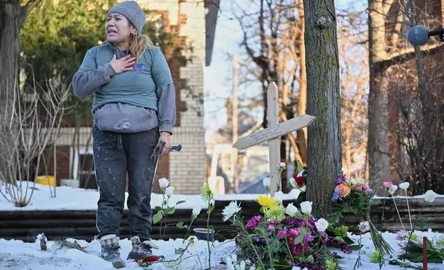 A protester stands next to a makeshift memorial honoring the victim of a fatal shooting involving federal law enforcement agents, near the scene in Minneapolis, Wednesday, Jan. 7, 2026. (AP Photo/Tom Baker)