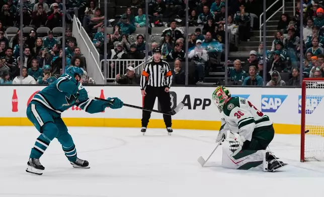 San Jose Sharks center Macklin Celebrini, left, scores against Minnesota Wild goaltender Jesper Wallstedt (30) in the shoot-out of an NHL hockey game, Wednesday, Dec. 31, 2025, in San Jose, Calif. (AP Photo/Godofredo A. Vásquez)