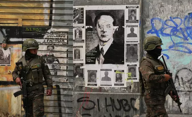 Soldiers stand guard in front of a poster of former President Jacobo Arbenz who was overthrown in a 1954 coup, near Congress in Guatemala City, Monday, Jan. 19, 2026, after President Bernardo Arévalo declared a state of emergency. (AP Photo/Moises Castillo)