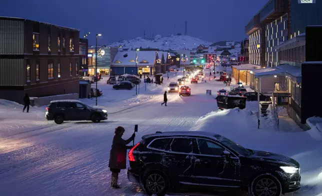 A woman cleans her car from snow in Nuuk, Greenland, on Monday, Jan. 12, 2026. (AP Photo/Evgeniy Maloletka)