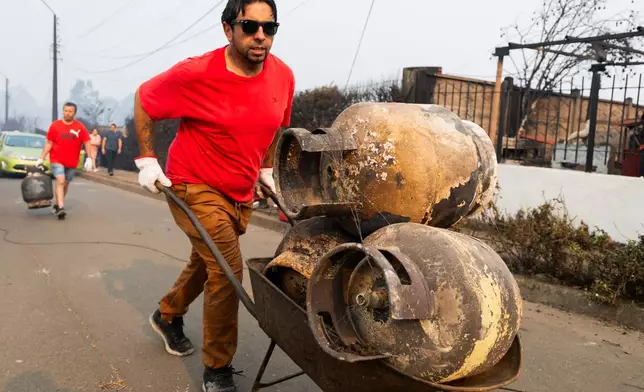 CORRECTS NAME TO VICTOR SILVA AND REMOVES ANDRES GARRIDO - Resident Victor Silva pushes a wheelbarrow with gas cylinders burned when wildfires destroyed homes in Tome, Chile, Monday, Jan. 19, 2026. (AP Photo/Javier Torres)