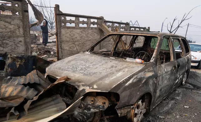 Andres Garrido carries burned roofing sheets at his home after it was burned by wildfires in Tome, Chile, Monday, Jan. 19, 2026. (AP Photo/Javier Torres)