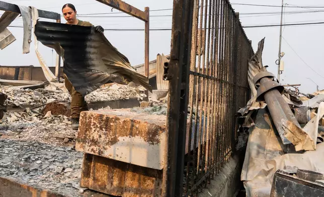A police officer clears burned roofing sheets from a home destroyed by wildfires in Tome, Chile, Monday, Jan. 19, 2026. (AP Photo/Javier Torres)