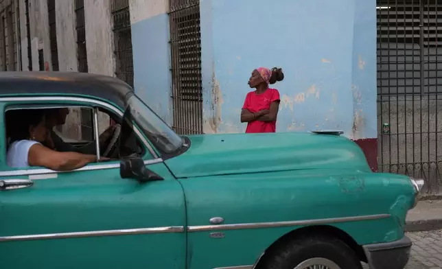 A woman gestures next to a classic American car in Old Havana, Monday, January 5, 2026. (AP Photo/Ramon Espinosa)