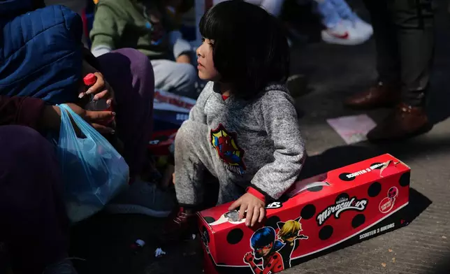 A child sits with their free gift at an event celebrating Three Kings Day, at the Angel of Independence in Mexico City, Monday, Jan. 5, 2026. (AP Photo/Marco Ugarte)