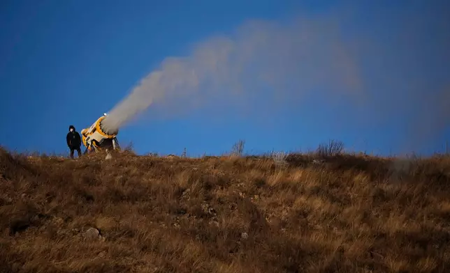 FILE - A person works at a snow making machine on a hill overlooking cross-country skiing practice before the 2022 Winter Olympics, Feb. 2, 2022, in Zhangjiakou, China. (AP Photo/Aaron Favila, File)