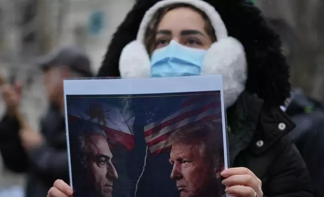 A protester holds up a poster showing Iran’s exiled crown prince Reza Pahlavi, left, and US President Danald J. Trump, right, as she demonstrates outside the House of Parliament, in London, England, Tuesday, Jan. 13, 2026. (AP Photo/Kin Cheung)