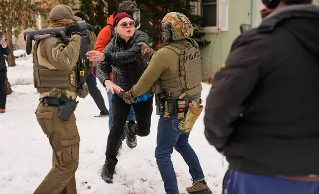 A woman gets into an altercation with a federal immigration officer as officers make an arrest Sunday, Jan. 11, 2026, in Minneapolis. (AP Photo/John Locher)
