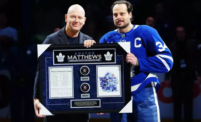 Former Toronto Maple Leafs player Mats Sundin, left, presents Auston Matthews (34) with artwork to recognize him on becoming the all-time franchise leader in goals prior to first period of an NHL hockey game against the Florida Panthers in Toronto, Tuesday, Jan. 6, 2026. (Frank Gunn/The Canadian Press via AP)