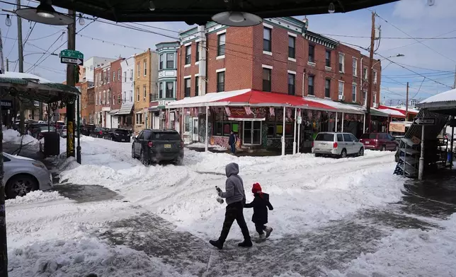 People cross a snow covered street in the aftermath of a winter storm in Philadelphia, Monday, Jan. 26, 2026. (AP Photo/Matt Rourke)