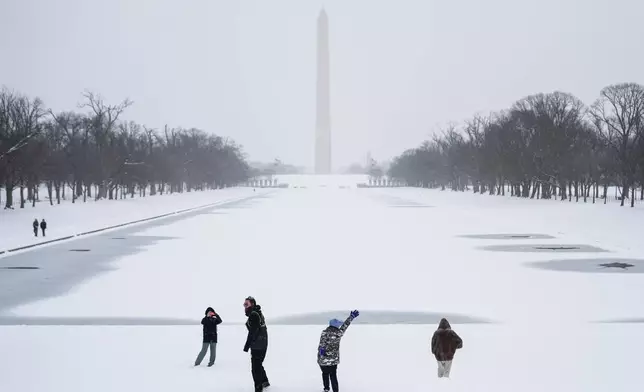 People walk along the National Mall as snow falls, Sunday, Jan. 25, 2026, in Washington. (AP Photo/Julia Demaree Nikhinson)