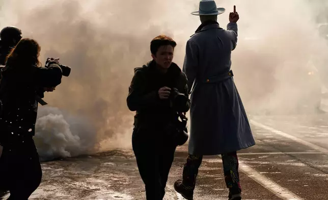 EDS NOTE: OBSCENITY - A man gestures as he walks toward a cloud of tear gas that was deployed by federal immigration officers Monday, Jan. 12, 2026, in Minneapolis. (AP Photo/John Locher)