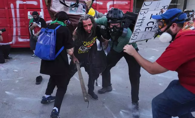 Protesters take cover from tear gas fired by federal police during clashes at the Metropolitan Detention Center in downtown Los Angeles on Friday, Jan. 30,2026. (AP Photo/Jae C. Hong)