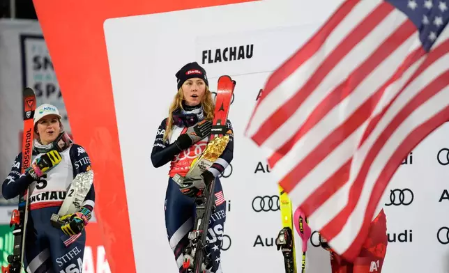 United States' Mikaela Shiffrin, center, winner of an alpine ski, women's World Cup slalom, listens to the national anthem with second placed United States' Paula Moltzan, in Flachau, Austria, Tuesday, Jan. 13, 2026. (AP Photo/Giovanni Auletta)