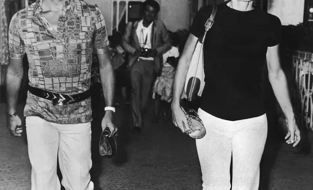 FILE - Jacqueline Onassis, walking barefoot, and Italian fashion designer Valentino Garavani, left, stroll the streets of the Island of Capri on the south side of the Gulf of Naples, Italy on August 31, 1970 after disembarking from her husband's, Greek shipping tycoon Aristotle Onassis, yacht "Christina". (AP Photo, File)