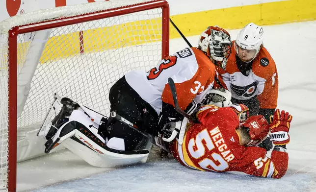 Philadelphia Flyers' Cam York, right, and Calgary Flames' MacKenzie Weegar, centre, crash into goalie Samuel Ersson during third period NHL hockey action in Calgary on Wednesday, Dec. 31, 2025. (Jeff McIntosh/The Canadian Press via AP)