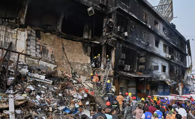 Firefighters carry remains of the victims after recovering from the rubble of a burnt building of a multi-story shopping plaza following a massive fire in Karachi, Pakistan, Monday, Jan. 19, 2026. (AP Photo/Ali Raza)