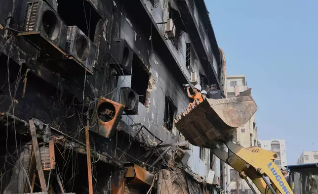 Firefighters search through a burnt building of a multi-story shopping plaza following a massive fire in Karachi, Pakistan, Monday, Jan. 19, 2026. (AP Photo/Ali Raza)