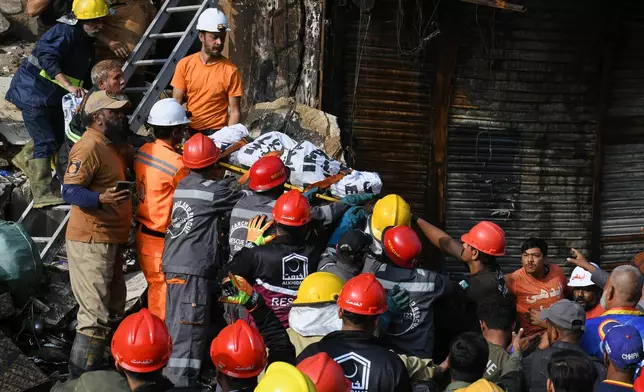 Firefighters transport a body after recovering from the rubble of a burnt building of a multi-story shopping plaza following a massive fire in Karachi, Pakistan, Monday, Jan. 19, 2026. (AP Photo/Ali Raza)