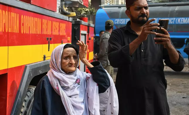 Family members of missing persons wait near the site of a burnt building of a multistory shopping plaza following a massive fire in Karachi, Pakistan, Monday, Jan. 19, 2026. (AP Photo/Ali Raza)
