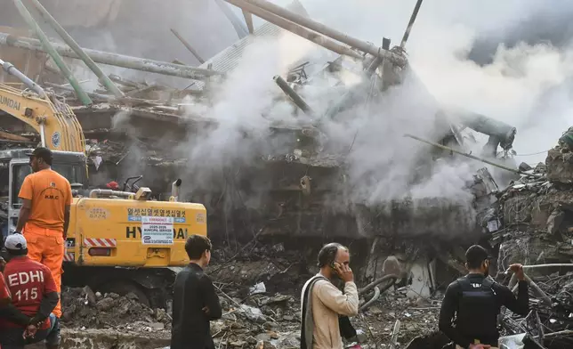 Rescue workers and firefighters use heavy machinery to search through the rubble of a burnt building of a multistory shopping plaza following a massive fire in Karachi, Pakistan, Monday, Jan. 19, 2026. (AP Photo/Ali Raza)