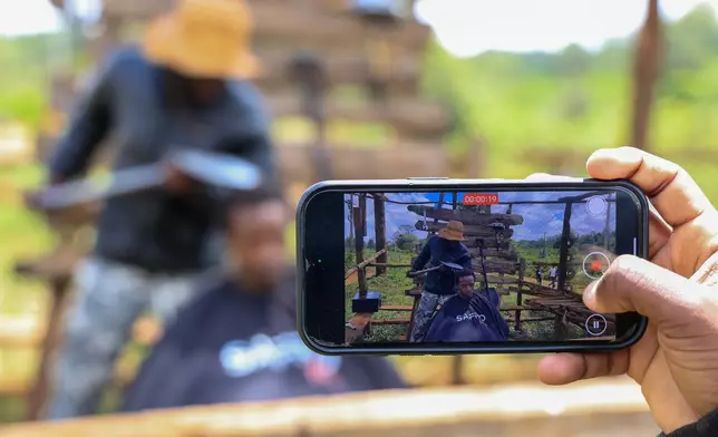 A man uses his phone to record barber and content creator Safari Martins as he shaves Ian Njenga in Kiambu, Kenya, Wednesday, Nov. 26, 2025. (AP Photo/Andrew Kasuku)
