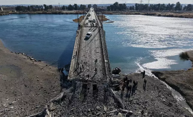 People cross the damaged Al-Rashid Bridge on foot, destroyed by retreating Syrian Democratic Forces (SDF) troops, a day after Syrian government troops took control of the area on the outskirts of Raqqa, northeastern Syria, Monday, Jan. 19, 2026. (AP Photo/Omar Albam)