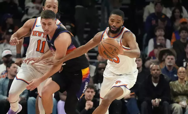 New York Knicks guard Mikal Bridges, right, steals the ball from Phoenix Suns guard Collin Gillespie, left, during the first half of an NBA basketball game, Friday, Jan. 9, 2026, in Phoenix. (AP Photo/Ross D. Franklin)