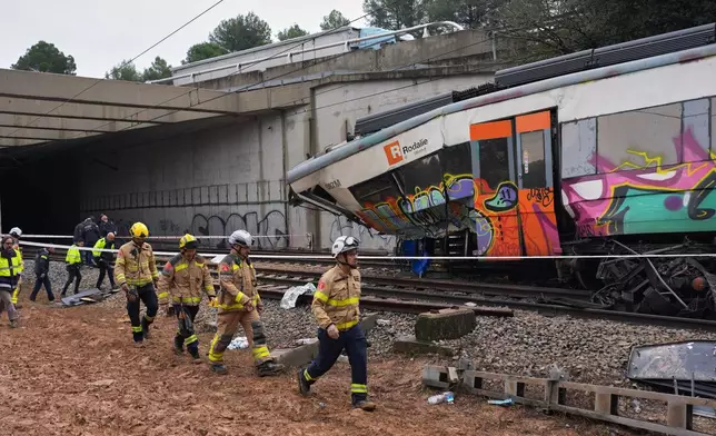 Police officers and firefighters inspect the damage after a commuter train derailed as a retaining wall collapsed onto the tracks in Gelida, near Barcelona, Spain, Wednesday, Jan. 21, 2026. (AP Photo/Joan Mateu Parra)