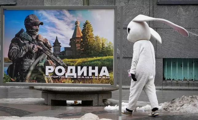 FILE - A street performer walks past a patriotic billboard showing a Russian serviceman and the slogan "The Motherland that we defend" in St. Petersburg, Russia, March 14, 2023. (AP Photo, File)