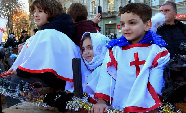 Georgian children take part in a religious procession to the Holy Trinity Cathedral to mark Orthodox Christmas in Tbilisi, Georgia, Wednesday, Jan. 7, 2026, with the building of Georgian Parliament on the left. (AP Photo/Shakh Aivazov)