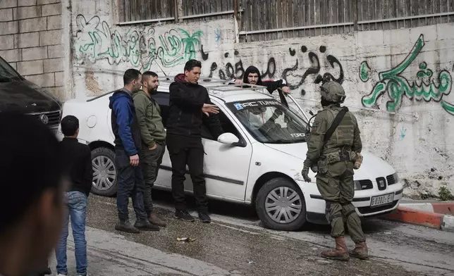 Palestinians speak with an Israeli soldier during an army raid in the West Bank city of Hebron Monday, Jan. 19, 2026. (AP Photo/Mahmoud Illean)