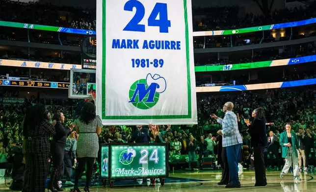 Former Dallas Mavericks player Mark Aguirre, second from front right, is joined by family as a banner is raised during his jersey retirement presentation at halftime during an NBA basketball game between the Mavericks and the Charlotte Hornets, Thursday, Jan. 29, 2026, in Dallas. (AP Photo/Jessica Tobias)