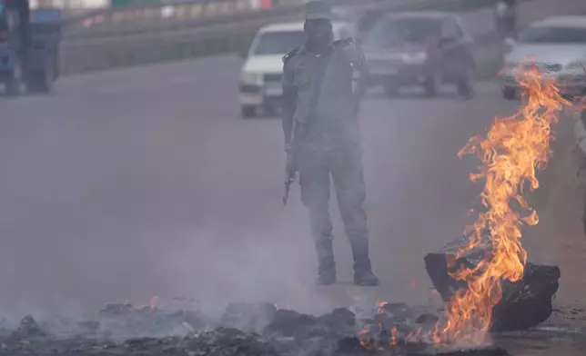 A Ugandan police officer makes a gesture behind a burning fire amid protests following the announcement of the preliminary results in Kampala, Uganda, Friday, Jan. 16, 2026. (AP Photo/Brian Inganga)