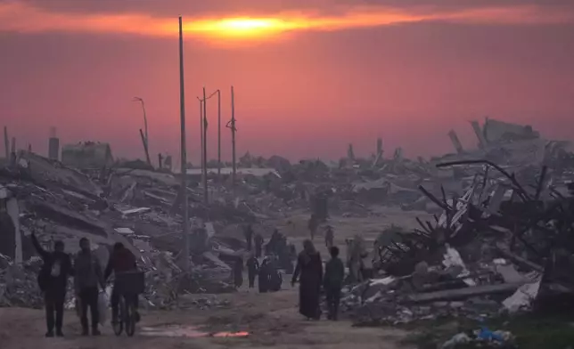 FILE - Palestinians walk through the ruins of destroyed buildings as the sun sets over Gaza City, Sunday, Jan. 4, 2026. (AP Photo/Jehad Alshrafi, File)
