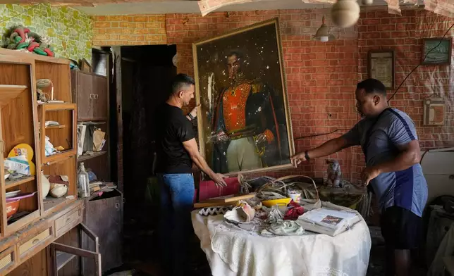 FILE - Jesus Linares, right, removes a painting of independence hero Simon Bolivar at his home, which he says was hit during U.S. military operations to capture Venezuelan President Nicolas Maduro, in Catia La Mar, Venezuela, Sunday, Jan. 4, 2026. (AP Photo/Matias Delacroix, File)